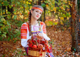 The girl sitting in autumn forest and holding a basket with apples