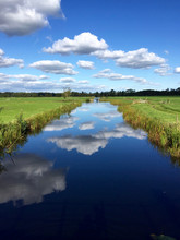 Dutch Canal And Grass Landscape/ Dutch Landscape With A Canal And Grass Fields With Mirror Reflection Of Clouds In Water