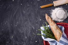 French Baguette With Rosemary Wrapped In A Towel In Red Basket And Whole Grain Flour, Rolling Pin On Rustic Background. Top View, Copy Space, Horizontal.