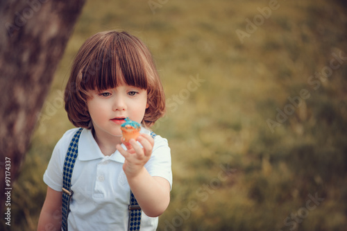 Cute Long Hair Toddler Boy Eating Cookie Outdoor On Summer Walk