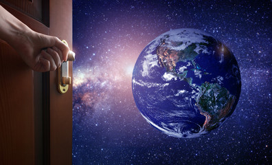 Wall Mural - hand opens empty room door to planet earth from the space. some