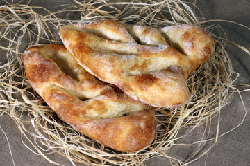 two white bread lying in straw on grey linen tablecloth