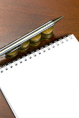 Wall Mural - Notepad with blank sheet and a pile of gold coins on the table