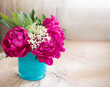 Violet peony flowers in blue vase on wooden table closeup with empty space background.