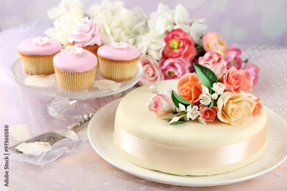 Cake with sugar paste flowers and cupcakes, on light background