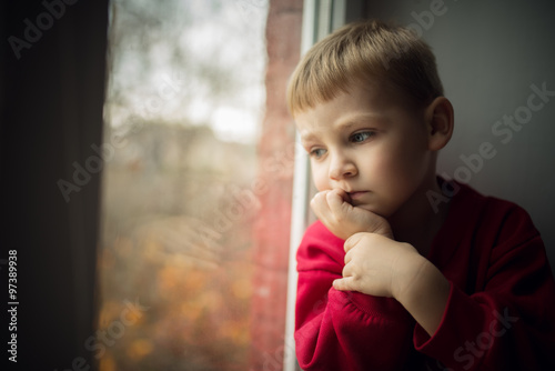 Fotografie, Obraz small boy sitting near window and thnking about something