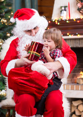 Wall Mural - Happy child with gift sitting on Santa Claus lap