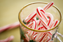 Gold Rimmed, Clear Glass Mug Filled With Small Candy Canes, Viewed From Above.  Gold Background.