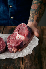 Tattoed hand offers a piece of meat stake above two steaks on cr