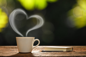 Cup of coffee with heart-shaped smoke and book in the garden