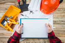 Construction Worker Architect Exploring Blueprints Plans For A New Building. Construction And Repair. Workplace Professional Holding In Hands White Plate, You Can Place Your Texts. Top View Work Table