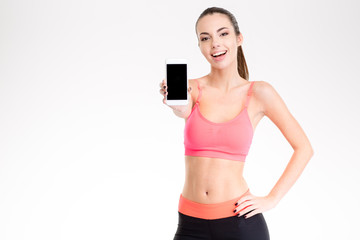 Attractive cheerful young fitness woman showing blank smartphone screen