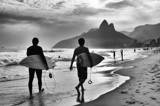 scenic black and white view of rio de janeiro, brazil with brazilian surfers walking along the shore