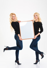 Attractive positive young blonde sisters twins posing with blank board