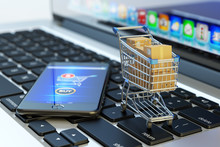 Online Shopping, Internet Purchases And E-commerce Concept, Modern Mobile Phone With Buy Button On The Screen And Shopping Cart Full Of Package Boxes On Computer Laptop Keyboard