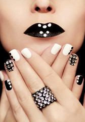 Multicolored manicure with white and black nail Polish decorated with rhinestones and a ring on his hand.