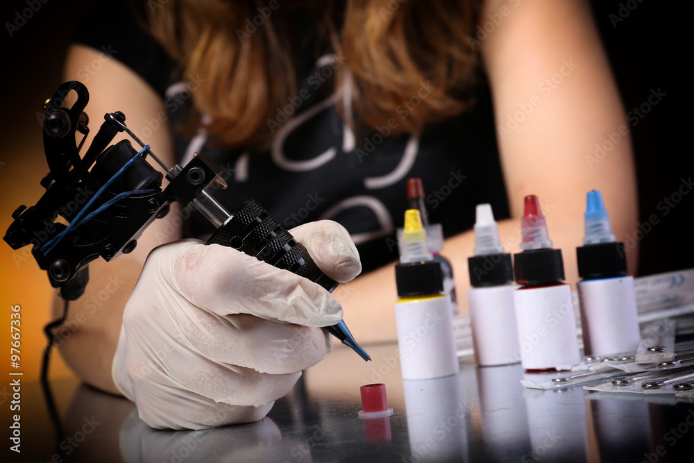 Tattoo machine in hand with red paint and needles on the table, close up
