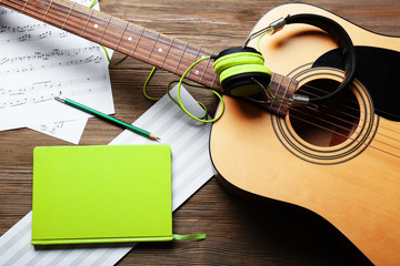 Classical guitar and headphones with music notes on wooden background