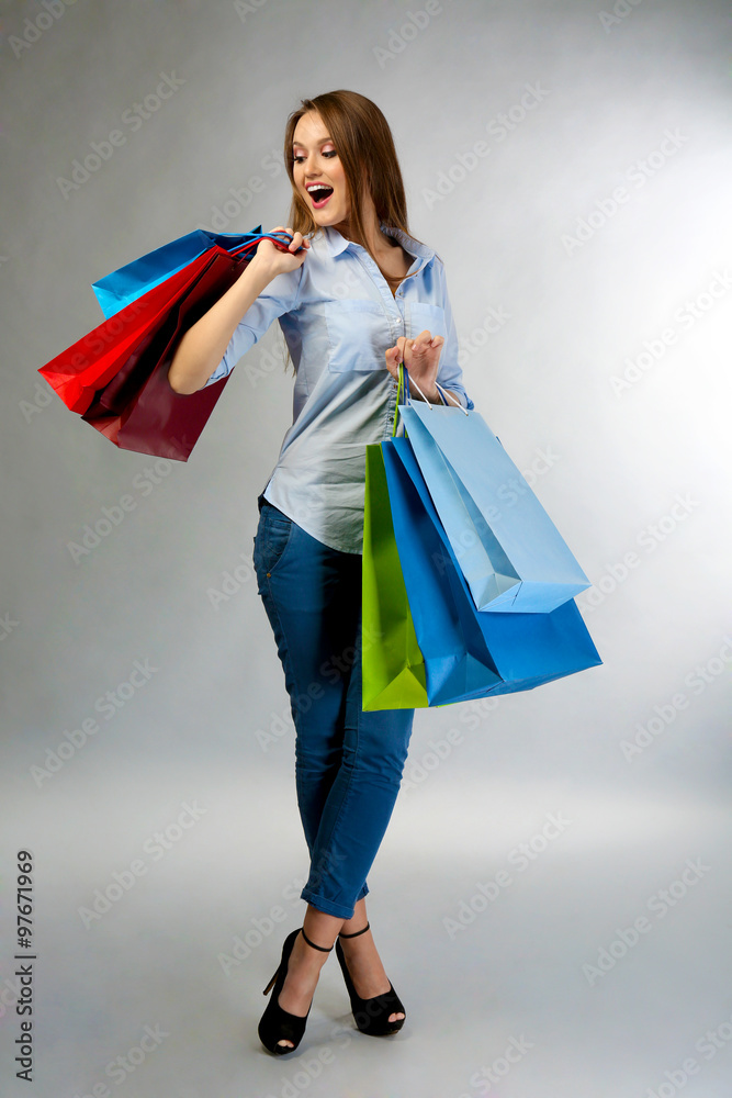 Young pretty woman with shopping packages on gray background