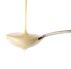 Condensed milk pouring from a spoon, isolated on white