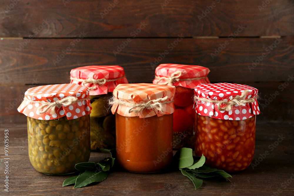 Jars with pickled vegetables and beans on wooden background
