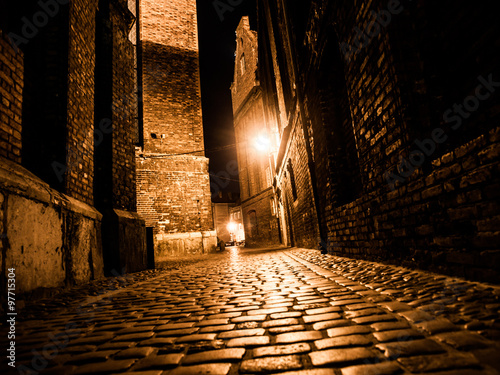 Fotomural Illuminated cobbled street in old city by night