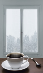 Wall Mural - A cup of coffee and snowstorm view from the window on the background