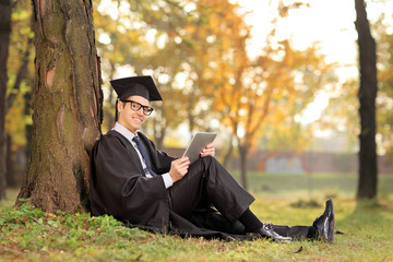 Canvas Print - Graduate student holding a tablet seated on grass