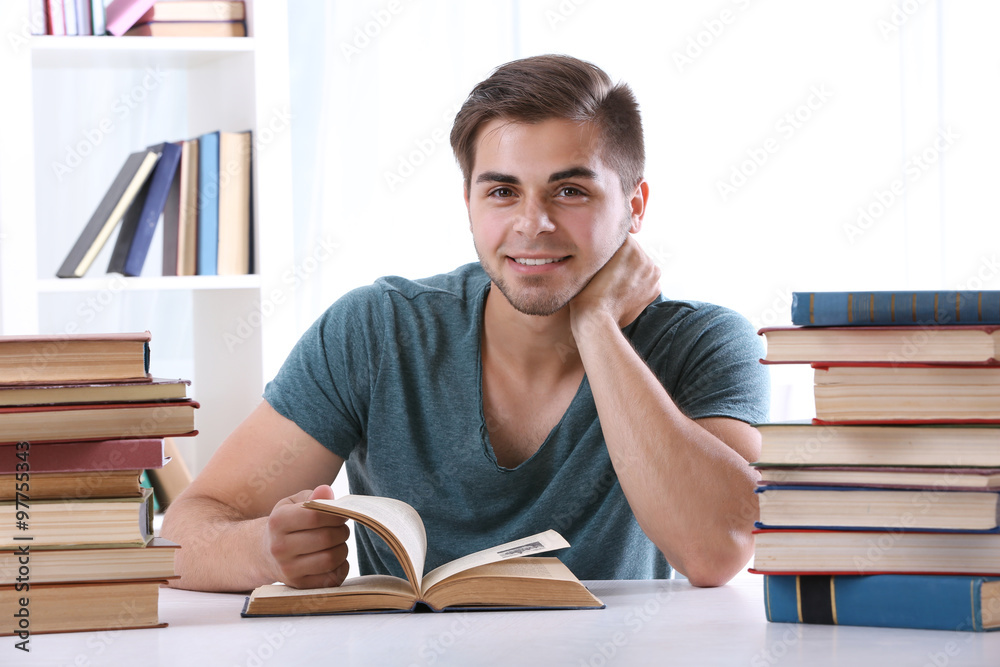 Young man reading book at table in room