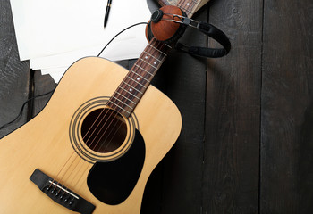 Poster - Acoustic guitar, headphones, musical notes and white papers on wooden background, close up