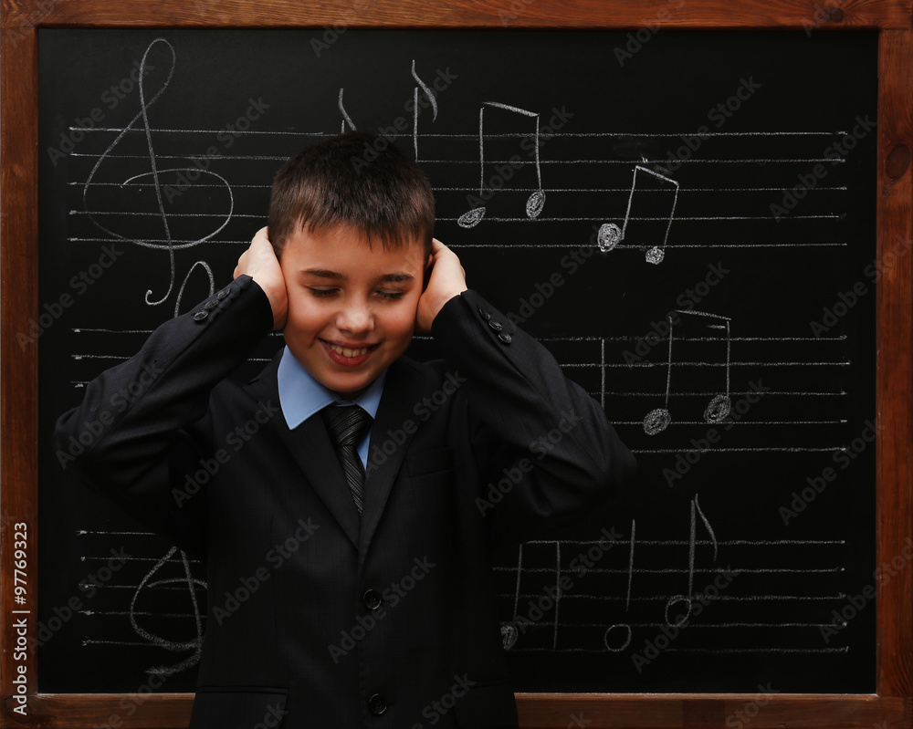 Young cute schoolboy standing at the blackboard with musical notes