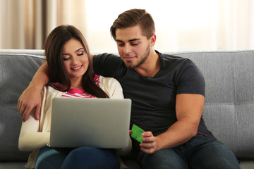 Canvas Print - Young happy couple using credit card with laptop at home on light background