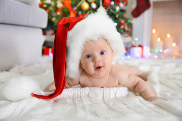 naked baby in red hat on the floor in the decorated christmas room