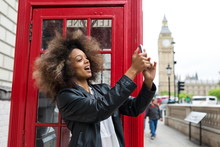 Young Woman Portrait Close To Red Telephone Box In London Taking Selfie.