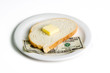 Slice of Bread with Money – A slice of bread sitting on a $10 bill. Concept for high cost of living, high cost of food, etc. On a white background.