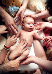 Newborn baby with big eyes being touched by hands of many family members. Symbol for love, care, protection, happiness.