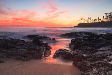 Long exposure of rocks and seaweed moss in waves, giving a mist like effect over ocean in Laguna Beach, California at sunset