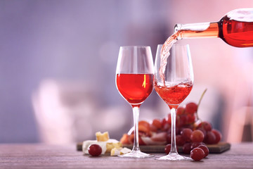 Canvas Print - Pouring pink wine from bottle into the wineglass on blurred background