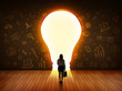 © ra2 studio - Business woman looking at bright light bulb in the wall