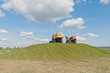 Weeled tractor rams green silo heap on blue sky background. 
