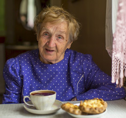 Elderly woman drinking tea with homemade cakes.