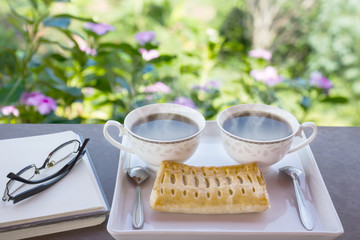 Two cups of hot black coffee with pie on white plate decorated w