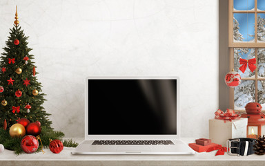 Laptop on table with isolated black screen for mockup in Christmas time. Christmas tree, gifts, decorations in background. 