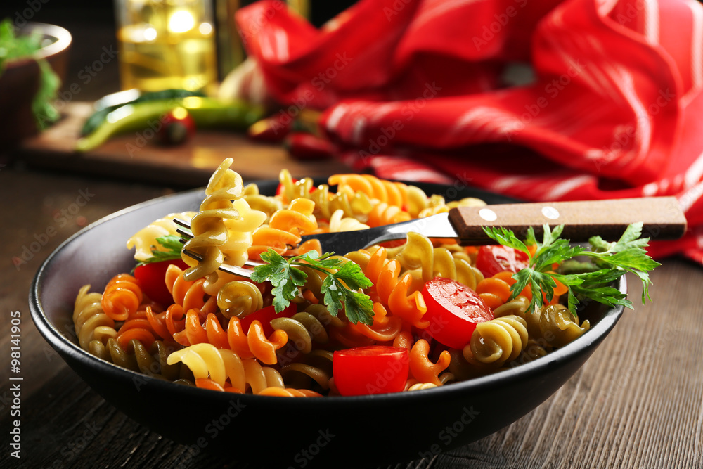 Delicious macaroni dish in black bowl on served wooden table