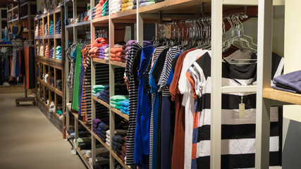 Various color sweatshirts at shelf and shirts on hangers in shop, Italy