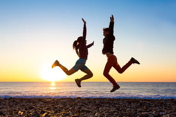 Wall Mural - Girl and Guy jumping high with arms up spectacular sunrise at ocean coast