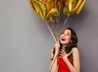 Surprised happy woman in red dress holding balloons