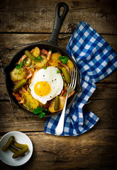 Wall Mural - country breakfast from potatoes, with bacon and fried eggs in a pig-iron frying pan. style rustic. selective focus