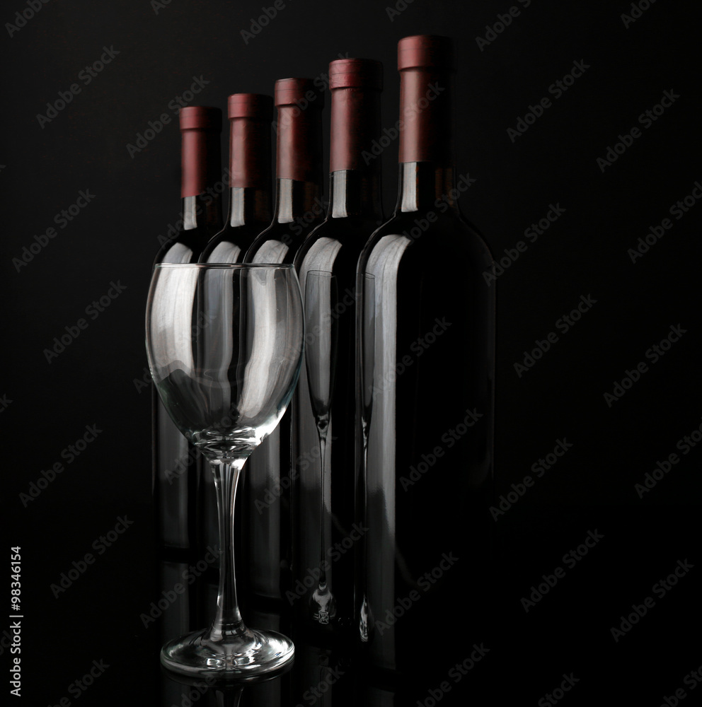 Glass and wine bottles in a row on black  background, close up