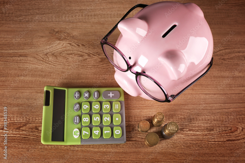 Piggy bank in glasses with calculator and coins on wooden background ...